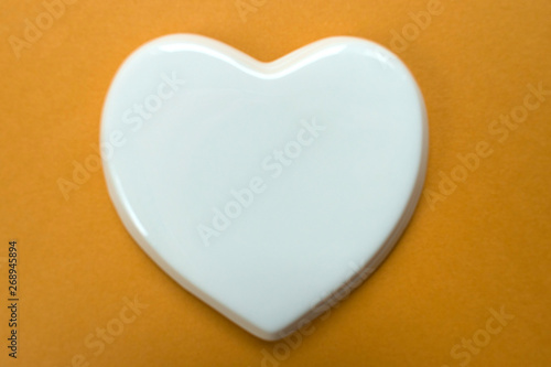 White glossy porcelain heart on a dark yellow background. Wedding card  A love note. Copy space