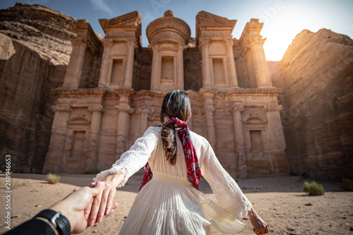 Asian woman tourist in white dress holding her couple hand at Ad Deir or El Deir, the monument carved out of rock in the ancient city of Petra, Jordan. Travel UNESCO World Heritage Site in Middle East