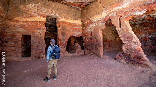 Asian man traveler standing in Dwellings homes or cave homes looking at abstract texture of rock in Petra ancient city of Jordan. Travel Middle East concept