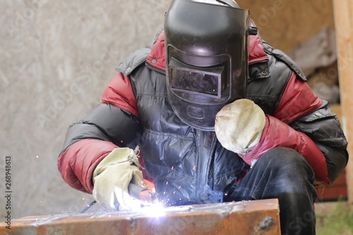 The worker in a mask of safety works with the welding machine.