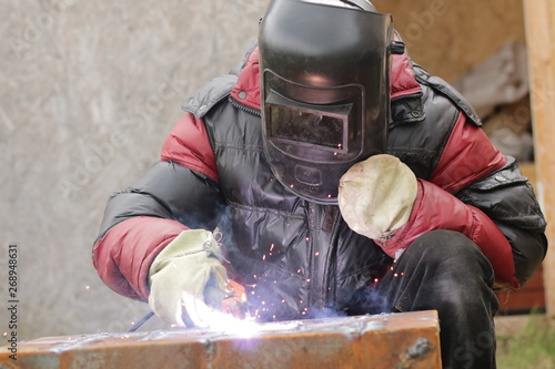 The worker in a mask of safety works with the welding machine.