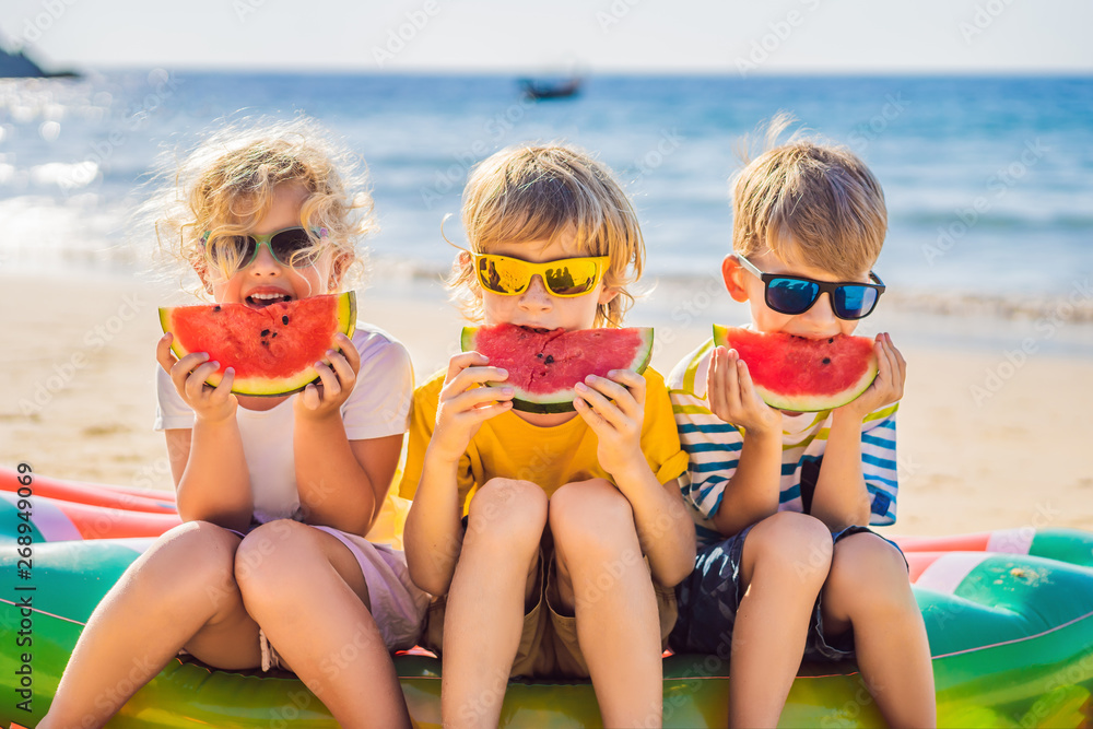 Children eat watermelon on the beach in sunglasses - obrazy, fototapety, plakaty 