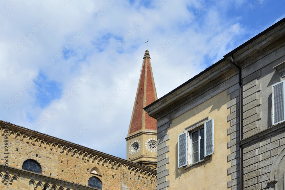 urban view of Arezzo historic center with an ancient building facade and the Cathedral in the background, under the cloudy and sunny sky