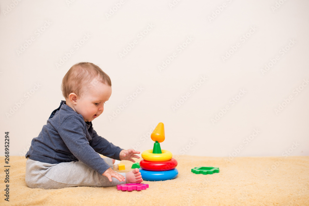 Cute baby playing with colorful toy pyramid in light bedroom. Toys for little kids. Child with educational toy. background with copy space Cute baby playing with colorful toy pyramid in light bedroom. Toys for little kids. Child with educational toy. background with copy space