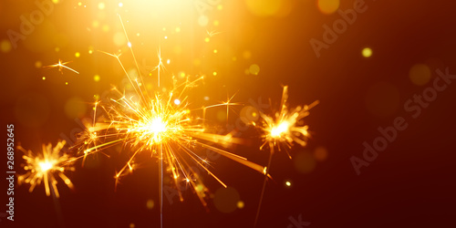 Glittering burning sparkler against golden bokeh background