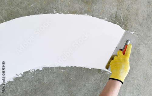 Hand with a spatula, the process of applying a layer of putty. Renovation of apartments. Repair the walls. Free space for advertising, text. photo