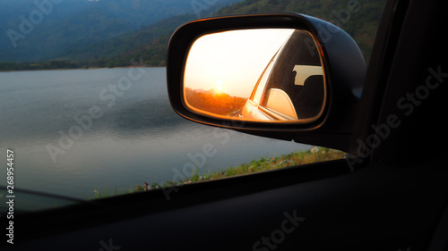 Orange landscape sunset reflect in mirror of car. Rear View Mirror Reflection on sun set. Road trip concept idea © Parichart