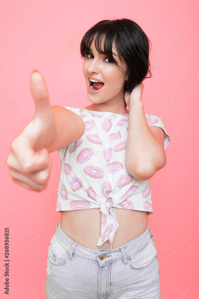 It's ok ! Portrait of a cheerful funny female showing thumb up looking at camera with open mouth touching her hair with a hand isolated over a pink wall. It's ok ! Portrait of a cheerful funny female showing thumb up looking at camera with open mouth touching her hair with a hand isolated over a pink wall.