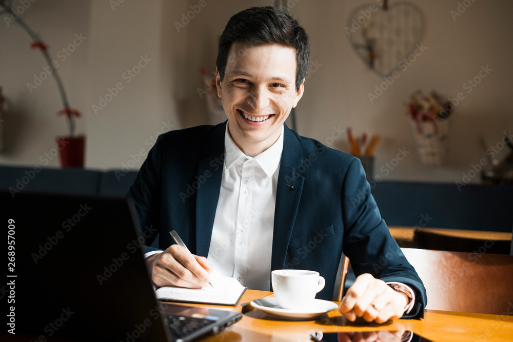 Portrait of a positive adult caucasian manager sitting at his working place while drinking a coffee and looking at camera smiling. Portrait of a positive adult caucasian manager sitting at his working place while drinking a coffee and looking at camera smiling.
