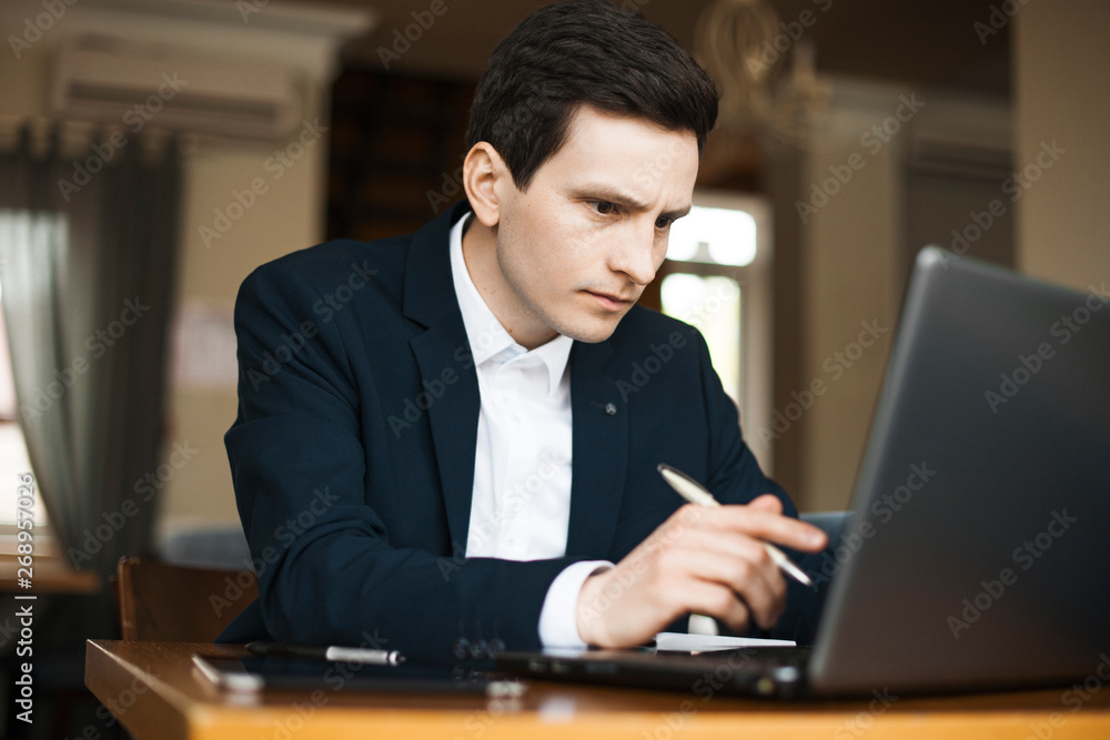 Close up portrait of a serious confident freelancer dressed in suit and working seriously at his laptop while sitting in a restaurant. Close up portrait of a serious confident freelancer dressed in suit and working seriously at his laptop while sitting in a restaurant.