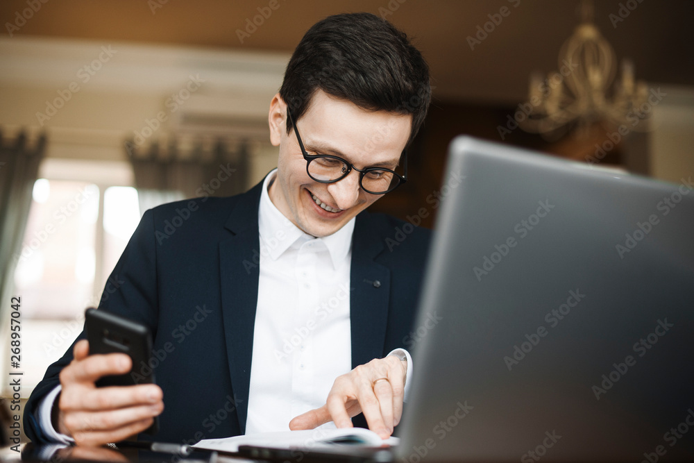 Adult caucasian worker doing paperwork smiling while holding a smartphone in his hand . Adult caucasian worker doing paperwork smiling while holding a smartphone in his hand .