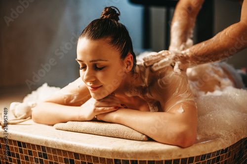 Pretty dark haired female having relaxing massage with foam in a wellness spa turkish hammam. photo