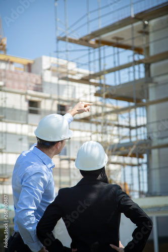 Two architects a man and a woman in construction in white helmets.