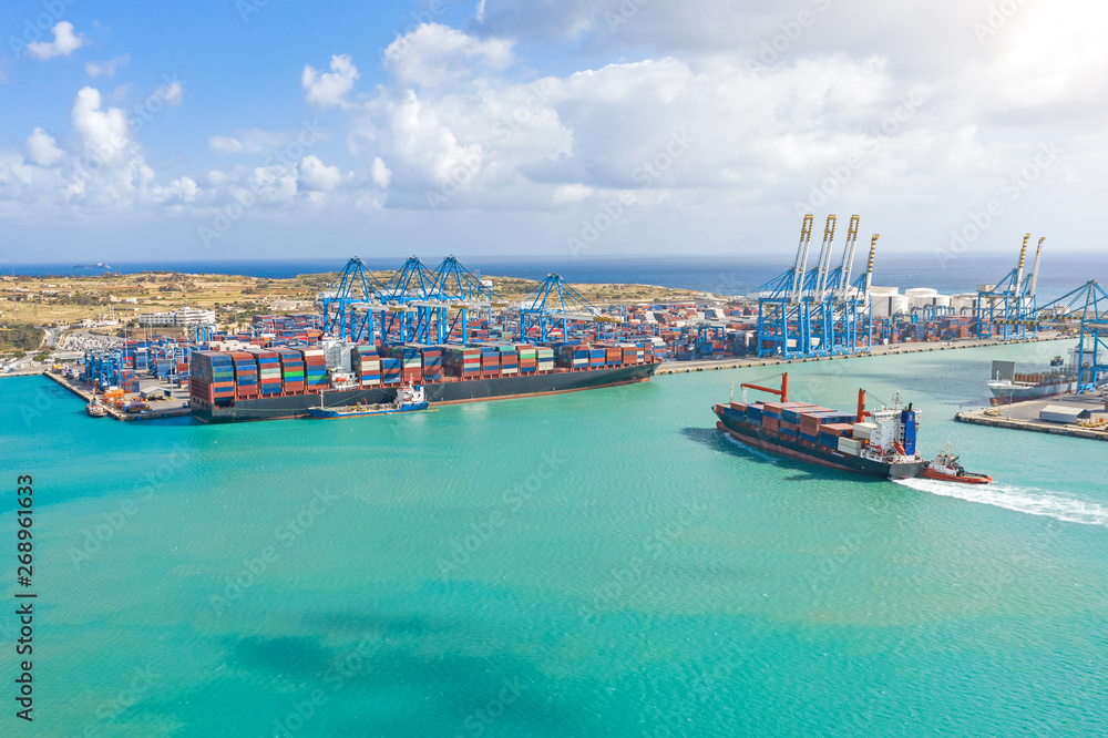 Aerial view from the height of a cargo harbor in a cargo seaport, a sailing ship with containers, and another one on the loading of goods.