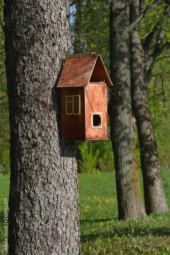 Brown nesting box in the form of a house on the background of trees and green foliage
