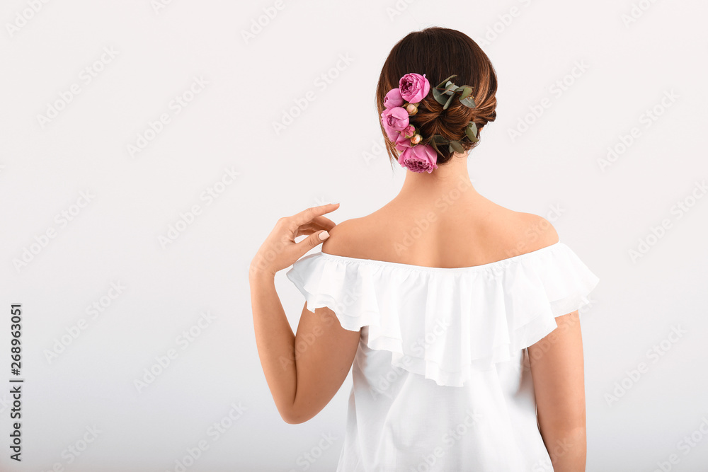 Young woman with beautiful flowers in her hair on light background, back view Young woman with beautiful flowers in her hair on light background, back view