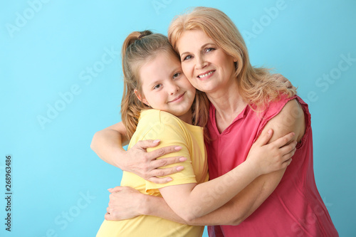 Mature woman and her cute granddaughter on color background