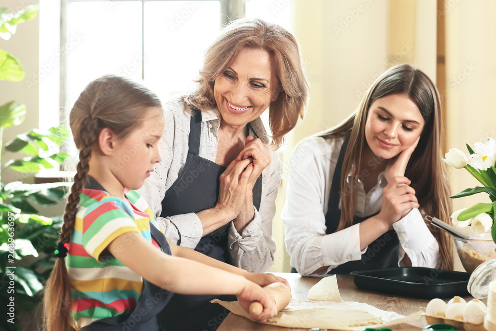 Little girl with her mother and grandmother cooking cookies in kitchen at home Little girl with her mother and grandmother cooking cookies in kitchen at home