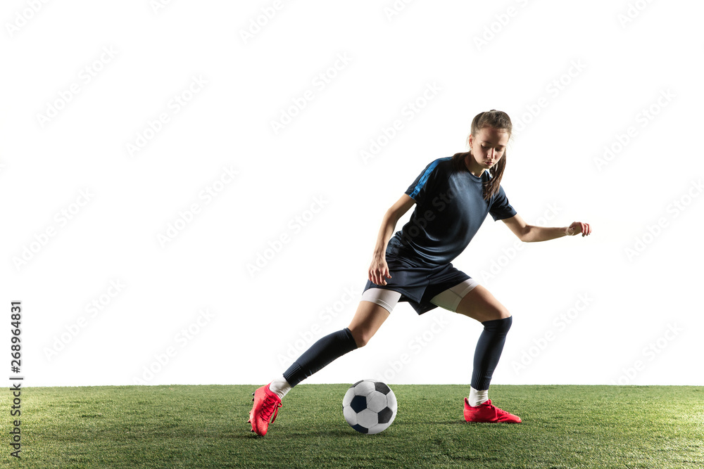 Obraz premium Young female football or soccer player with long hair in sportwear and boots kicking ball for the goal in jump isolated on white background. Concept of healthy lifestyle, professional sport, hobby.