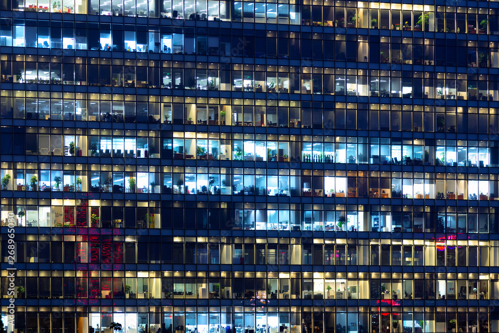 Office building exterior in the late evening with interior lights. Business people working in the evening. Illuminated office building Office building exterior in the late evening with interior lights. Business people working in the evening. Illuminated office building