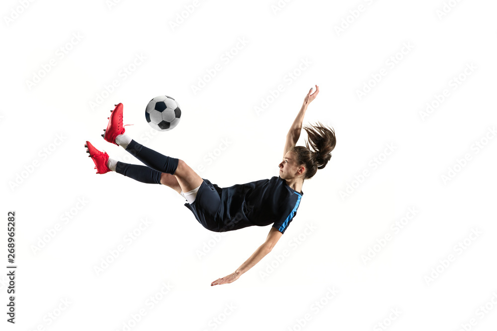 Fototapeta premium Young female football or soccer player with long hair in sportwear and boots kicking ball for the goal in jump isolated on white background. Concept of healthy lifestyle, professional sport, hobby.