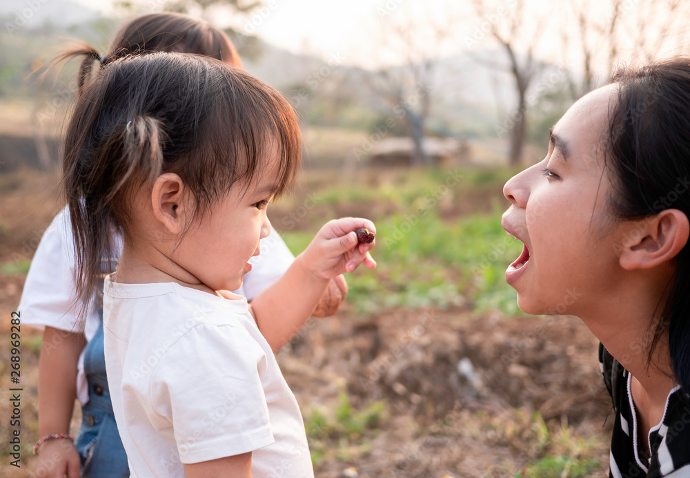 Asian little girl feeding fresh mulberry ball with finger to mother in the garden with sunset background. Playing is learn for children. Asian little girl feeding fresh mulberry ball with finger to mother in the garden with sunset background. Playing is learn for children.