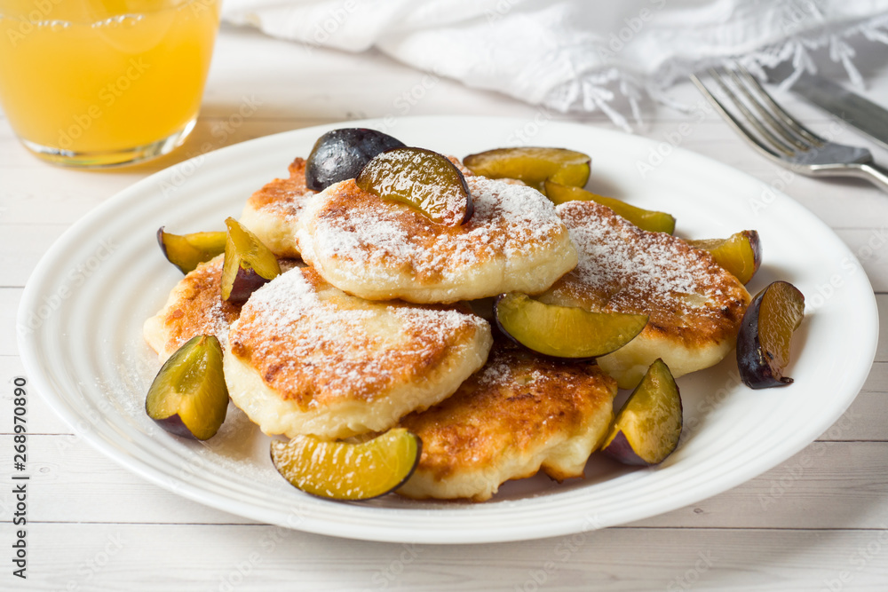 Cheese pancakes in powdered sugar with fresh plums on a plate