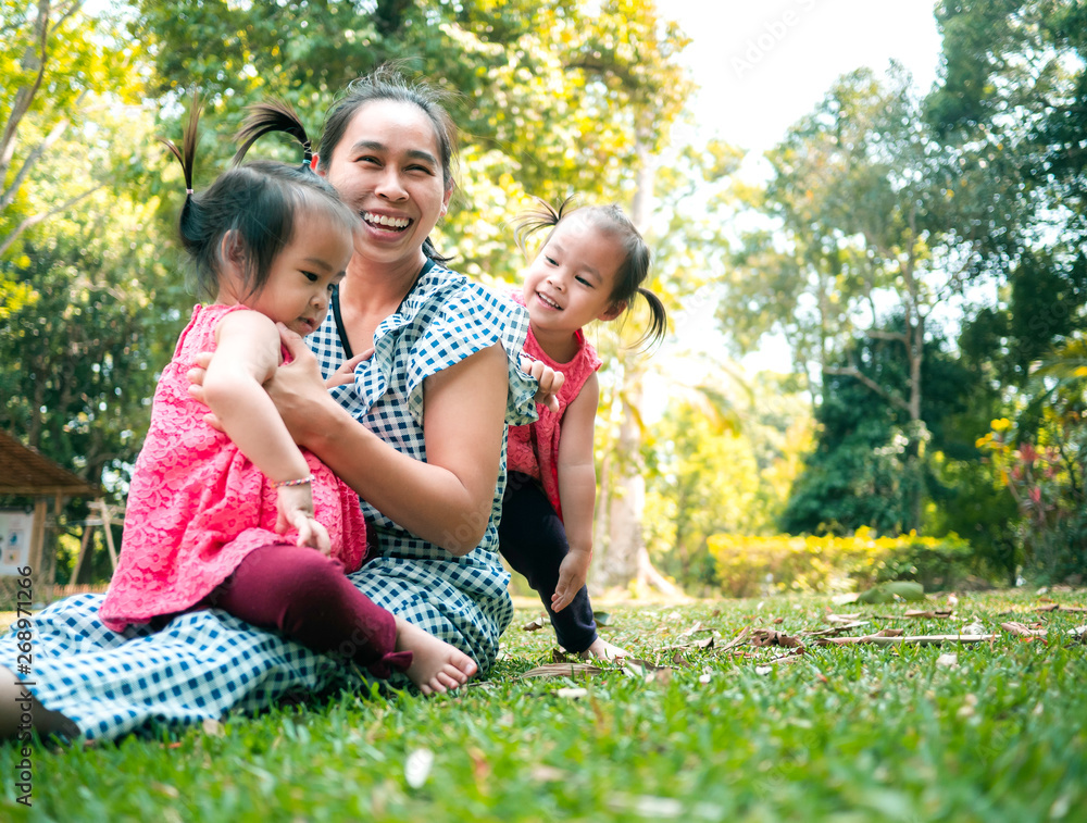 Fototapeta premium Asian mother and her daughters playing together on grasses ground in the park so happily.