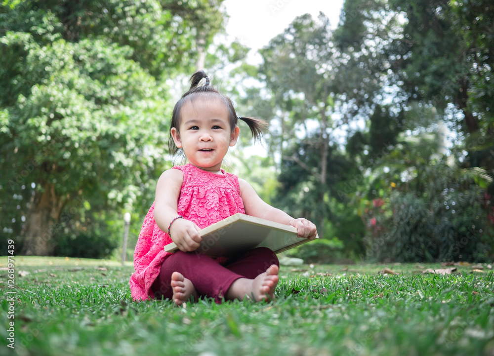 Asian little girl holding empty white board and sitting on grasses ground. Space for write your text. Asian little girl holding empty white board and sitting on grasses ground. Space for write your text.