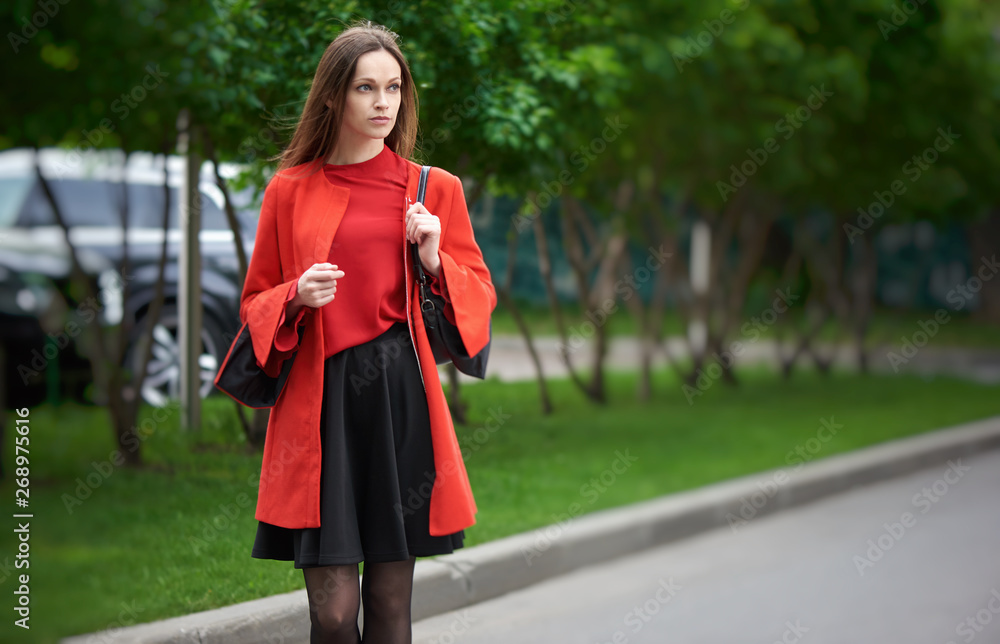 Fototapeta premium Beautiful brunette young woman wearing red jacket and walking on the street