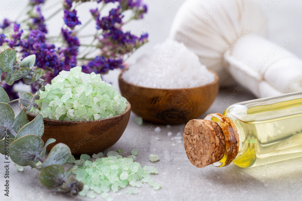 Sea salt in bowl, aroma oil in bottles, Wellness and flowers on grey textured background and flowers on vintage wooden background. Selective focus. Sea salt in bowl, aroma oil in bottles, Wellness and flowers on grey textured background and flowers on vintage wooden background. Selective focus.