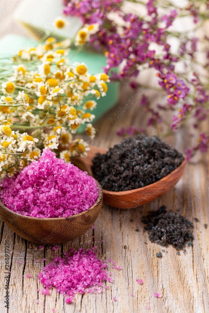 Fototapeta premium Sea salt in bowl, aroma oil in bottles, Wellness and flowers on grey textured background and flowers on vintage wooden background. Selective focus.