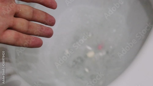 Slow motion men's hand with palm throws a lot of white pills into the toilet top view. close-up