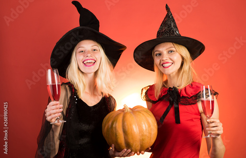 Two beautiful women in carnival sexy costumes of witches. Isolated image. Two happy young women in black and red dresses, costumes witches halloween on party over orange background.
