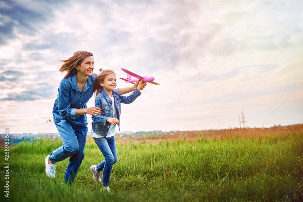 Young woman and girl in denim clothes having fun with small plane on green lawn in summer day Young woman and girl in denim clothes having fun with small plane on green lawn in summer day
