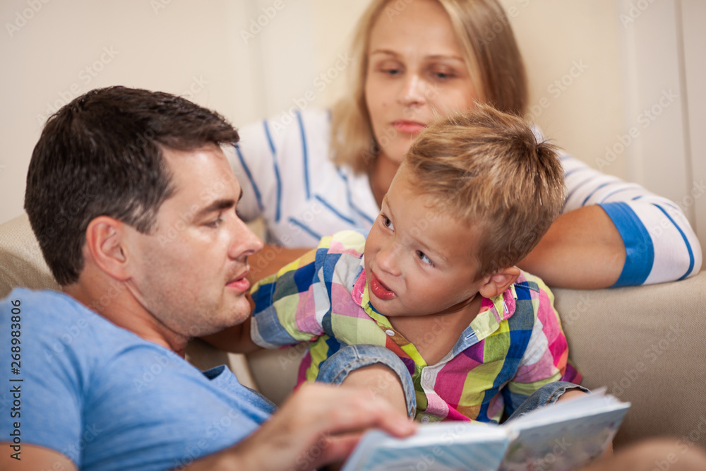 Little boy looking at father with curiosity during the evening book reading with a family
