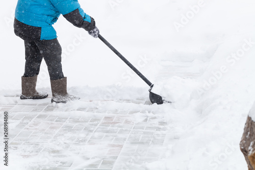Old woman in warm blue jacket clears a snowdrifts with a snow shovel