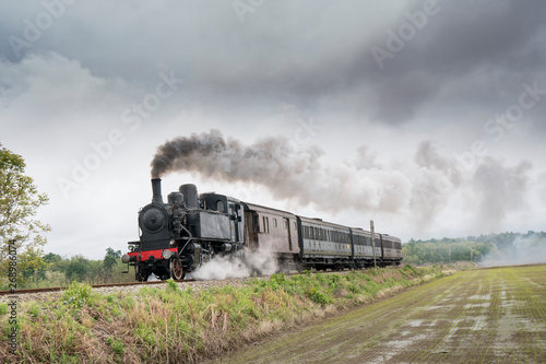Vintage steam train with ancient locomotive and old carriages runs on the tracks in the countryside