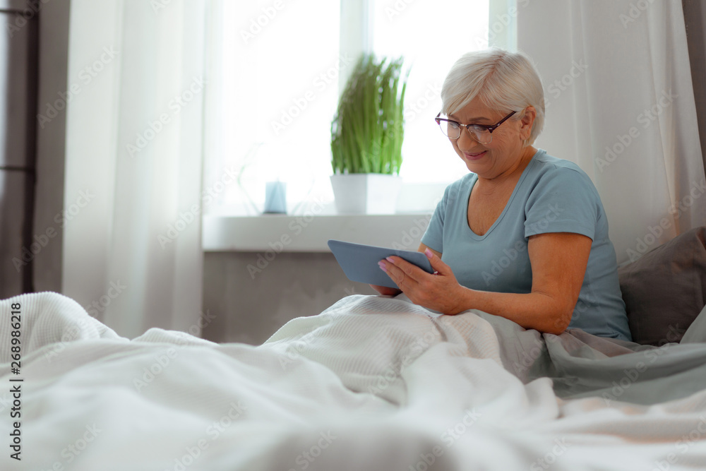 Smiling female clicking on the tablet while lying in bed Smiling female clicking on the tablet while lying in bed
