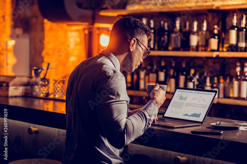 Obraz na plátne Businessman owning bar working on laptop and drinking coffee