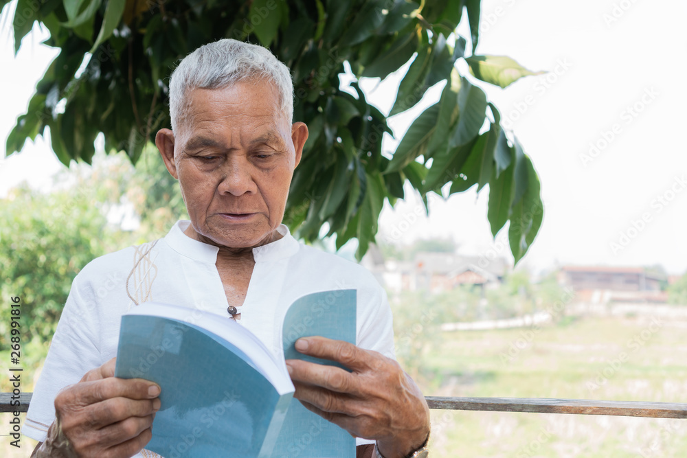 Adult education Learning Studying concept : Happy Asian Elderly retired man sitting reading book at garden home outdoor for learning or relax by self Adult education Learning Studying concept : Happy Asian Elderly retired man sitting reading book at garden home outdoor for learning or relax by self