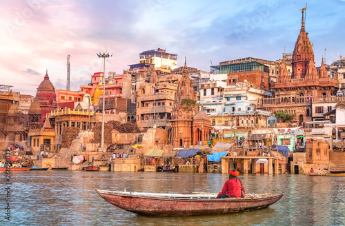 Ancient Varanasi city architecture at sunset with view of sadhu baba enjoying a boat ride on river Ganges. photo