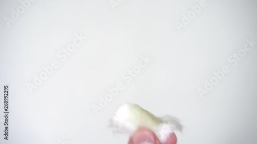 female hands on a white background are holding a cotton pad and drench it with green nail polish remover without acetone