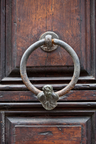 Ancient italian door knocker on wooden brown door.