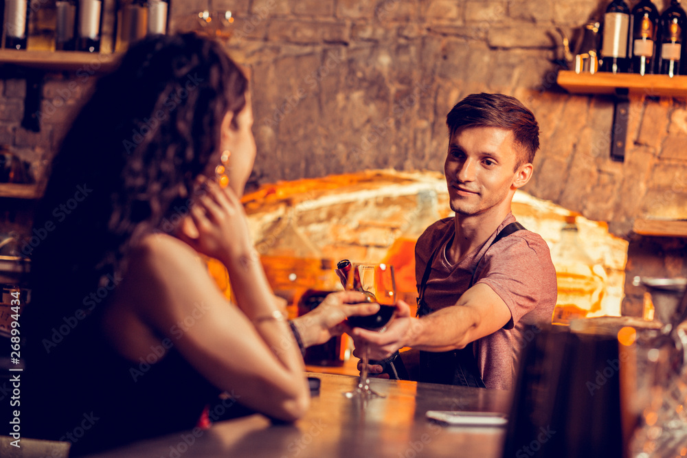 Barman giving glass of wine to dark-haired client