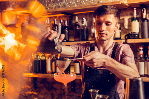 Barman pouring juice thorough sieve while making cocktail
