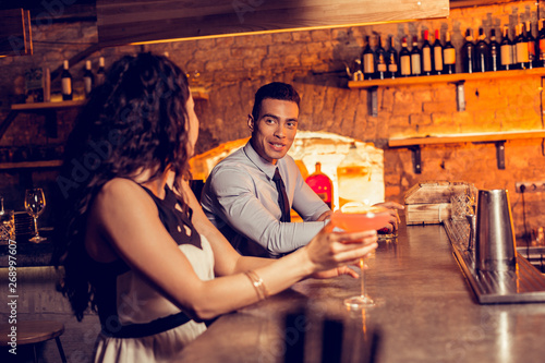 Curly woman drinking cocktail in bar talking to man photo