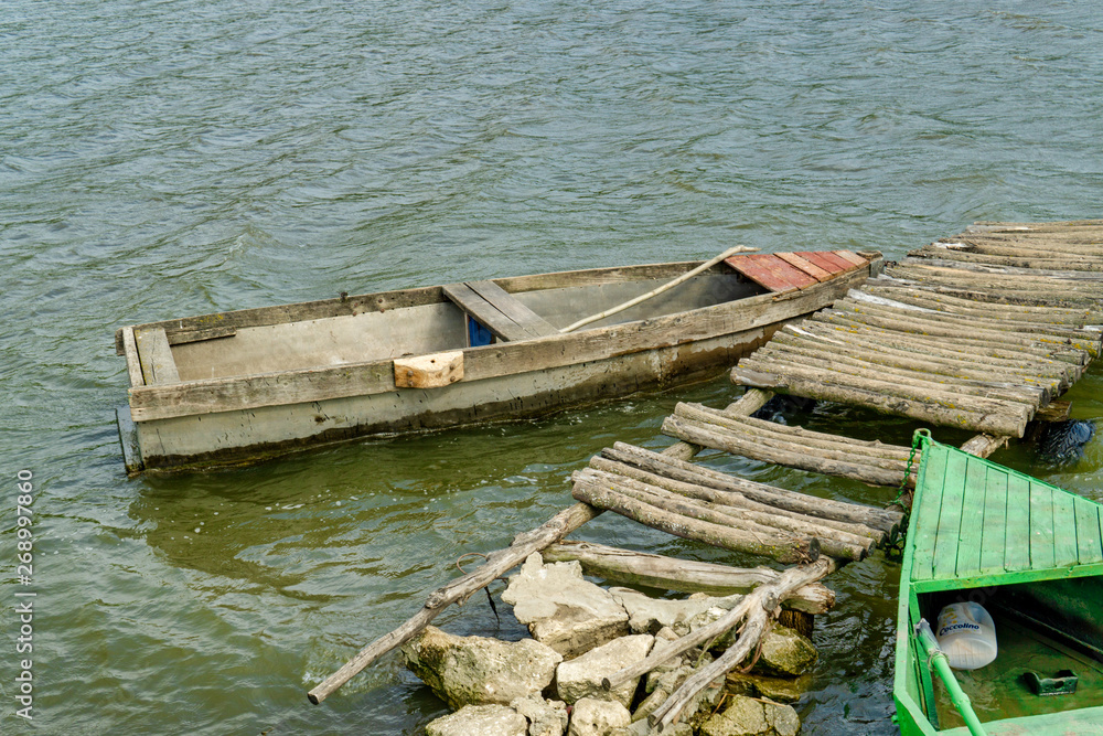 Old Wooden Rowing Fishing Boat Moored Near Lake Or River Coast In Beautiful Sunny Day Old Wooden Rowing Fishing Boat Moored Near Lake Or River Coast In Beautiful Sunny Day