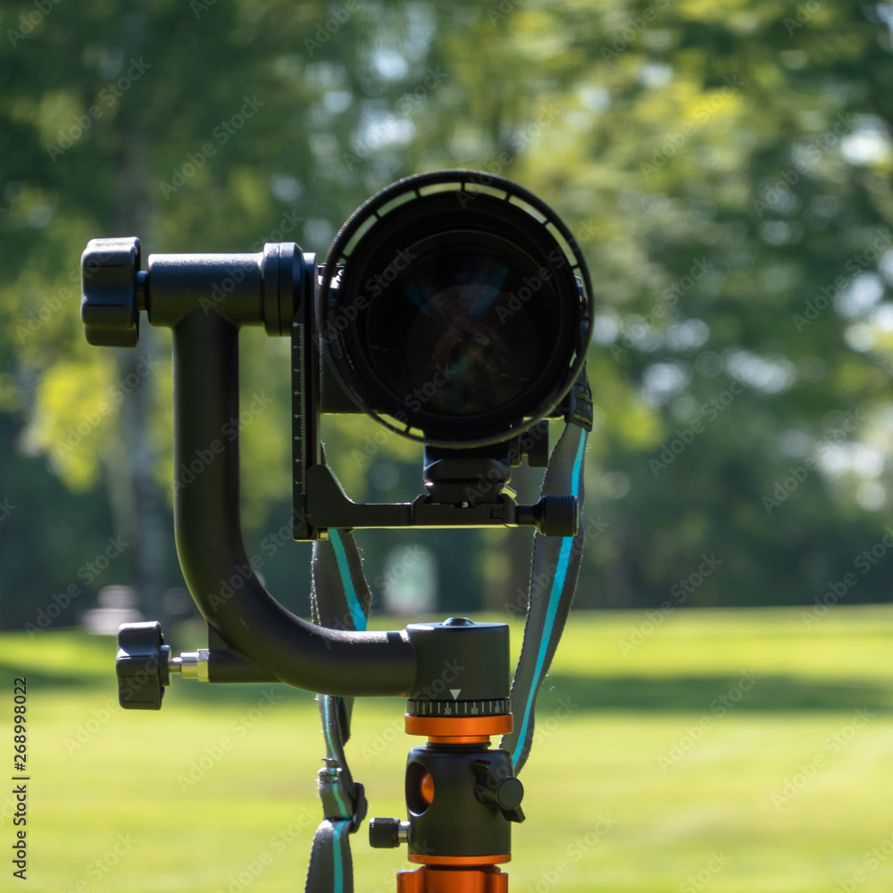 Front shot of a large telephoto lens mounted outdoors on a tripod with manual heavy gimbal, intentionally blurred background, hobby