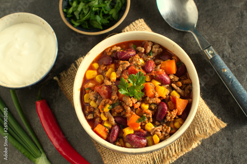 Chili con carne in a rustic bowl on a grey stone background- traditional dish of mexican cuisine